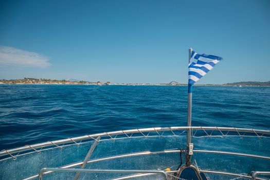 Flag of Greece waving over the see on cruise sheep in front of beautiful coastline