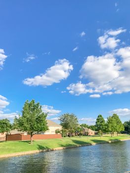 Beautiful waterfront house with row of mature bold cypress trees in suburbs Dallas, Texas, USA. Suburban single family detached home along river with high stone retaining wall, green grass lawn