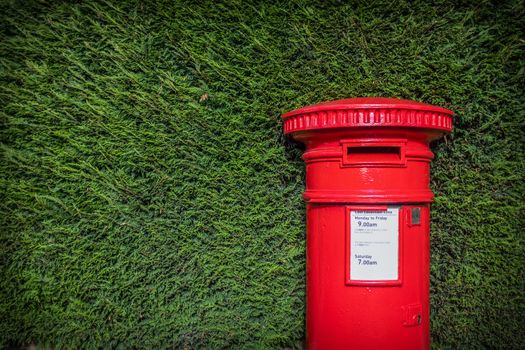 A Striking Red British Post Box Set Against A Neat Green hedgerow In England