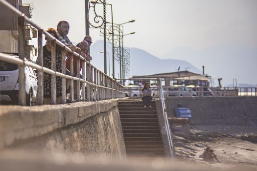 People standing on the railing watching the sea at sunset