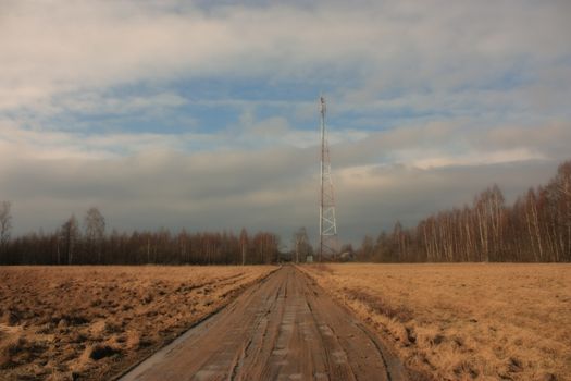 view of the communications tower and road to the forest, against a blue sky with white clouds