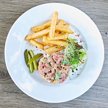 Meat tartar made of raw beef, egg yolk, tomato, sauce and herbs and served with french fries and vegetable salad