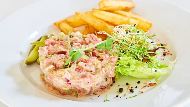 Meat tartar made of raw beef, egg yolk, tomato, sauce and herbs and served with french fries and vegetable salad