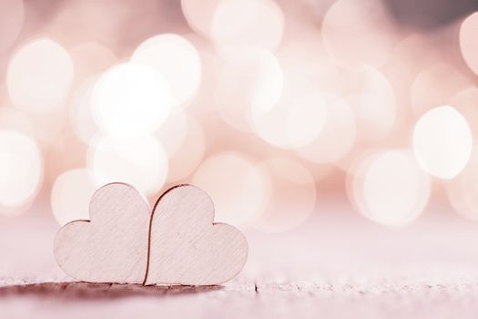Two wooden hearts on pink glowing bokeh hearts background for Valentines day