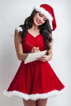 Pretty smiling pin-up Santa girl with wish list and pen
