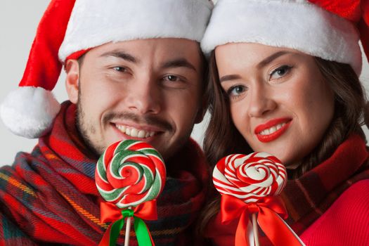 Young happy smiling couple in christmas santa hats with lollipops
