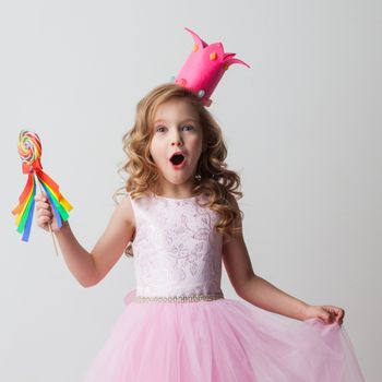 Beautiful little candy princess girl in crown holding big lollipop and smiling