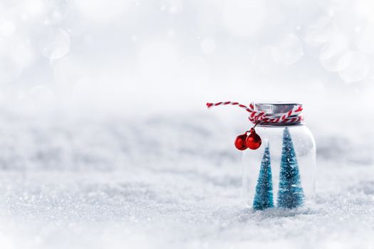 Christmas ornaments of glass jar with striped ribbon , bells and fir trees inside on snow background