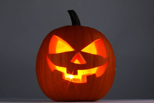 Glowing Halloween pumpkin head jack lantern on gray background