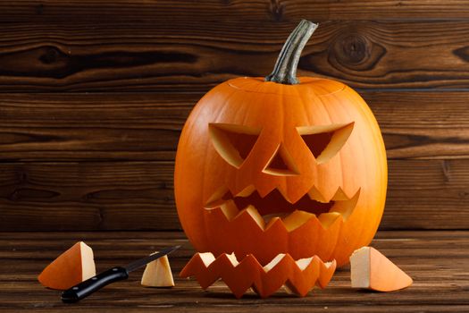 Carving of Halloween pumpkin in progress, pieces and cutting knife on wooden background