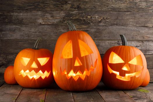 Three Halloween pumpkins head jack o lantern and candles on wooden table background