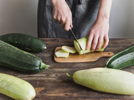 Zucchini harvest. Woman slices zucchini on wooden table. Farm organic zucchini harvesting