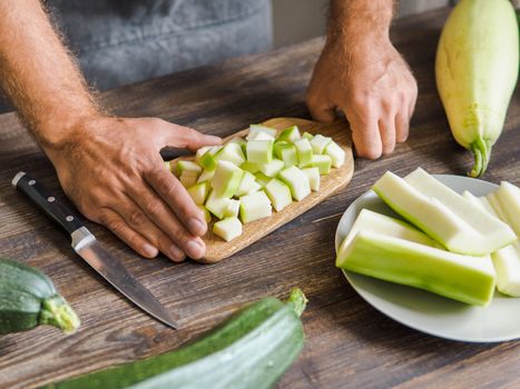 Zucchini harvest. Man slices zucchini cubes for freezing on wooden table. Farm organic zucchini harvesting