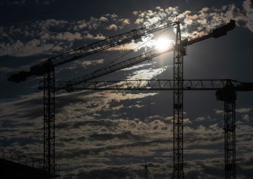 Cranes on a construction site with a cloudy sky during sundown