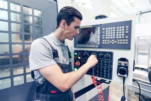 Worker pressing programming buttons on CNC machine control board in factory