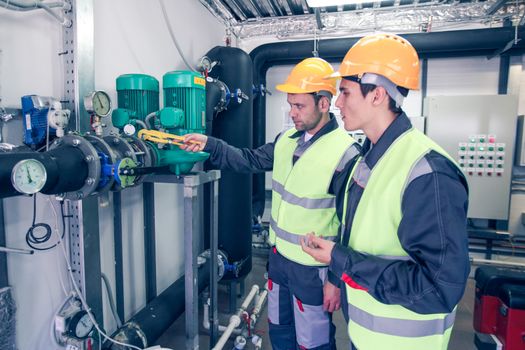 Two workers in hardhats at plant checking parameters of pressure