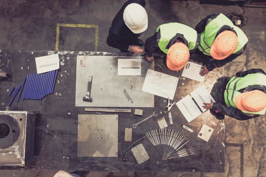 Workers and manager in safety helmets working with documents at factory