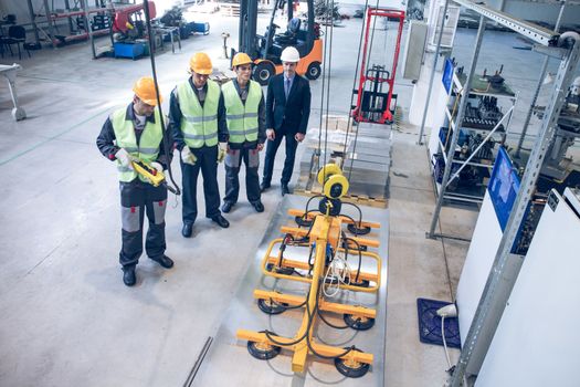 Workers near metal sheet lifting device at factory