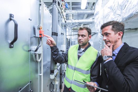 Worker and manager in electrical switchgear room of CNC plant