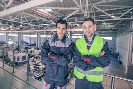 Team of two workers in uniform standing at background of CNC factory