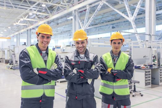 Team of three workers in uniform standing at background of CNC factory