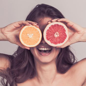 Funny playful young woman holding halves of citrus fruits against her eyes