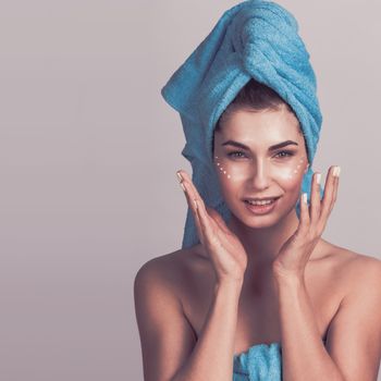 Beautiful woman with towel on head applying creme after shower