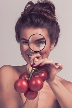Young beautiful woman female inspecting testing tomato food with magnifying glass