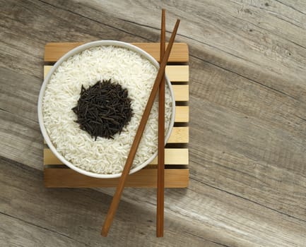 two varieties of rice, white in a round bowl, and black in a wooden spoon with brown chopsticks.