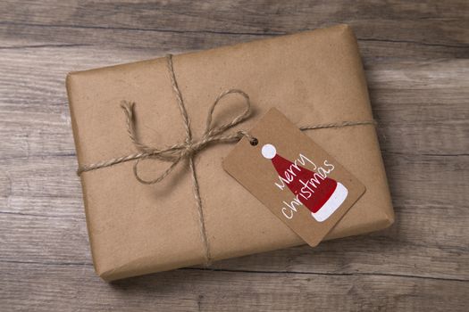 Christmas or New Year gift box wrapped in kraft paper with blank gift tag on old wooden background.