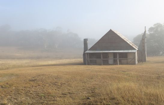 Log hut in Snowy Mountains with early morning fog across the landscape.  The huts are basic made of strong timbers, corrugated iron and ceilings of calico