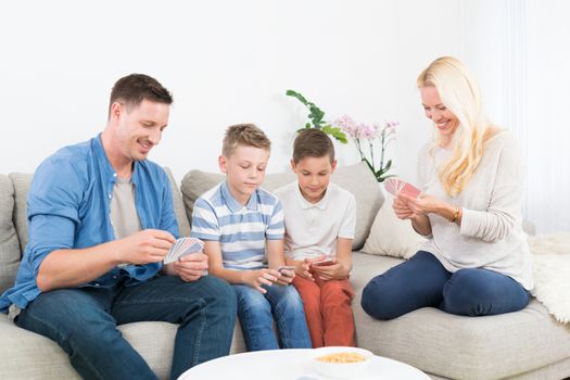 Happy young family playing card game on living room sofa at home. Spending quality leisure time with children and family concept.