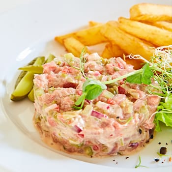 Meat tartar made of raw beef, egg yolk, tomato, sauce and herbs and served with french fries and vegetable salad