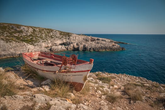The old abandoned wooden fishing boat on a rocky cliff shore on a sunny day in greece , Zakynthos.
