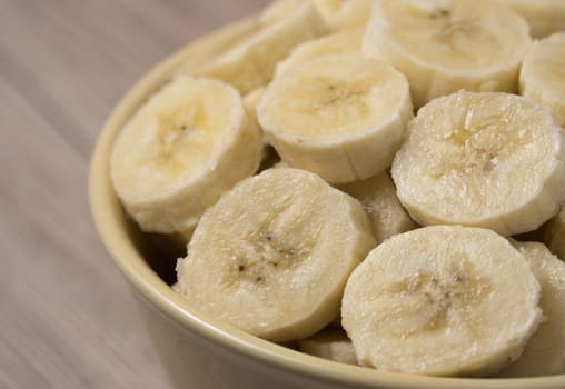 Fresh ripe organic sliced bananas in a ceramic bowl on a wooden table.