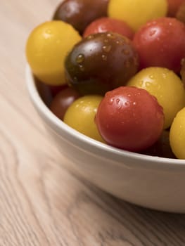 Cherry tomatoes in a variety of colors in ceramic bowl on wooden background.