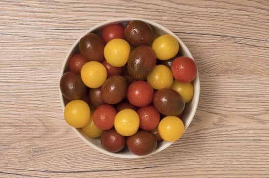 Cherry tomatoes, red,yellow and kamato in ceramic bowl on wooden background. Top view.
