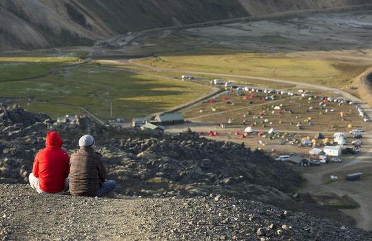 Camping tents in a mountain valley and two tourist on the rock in the foreground