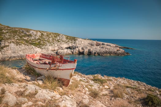 The old abandoned wooden fishing boat on a rocky cliff shore on a sunny day in greece , Zakynthos.