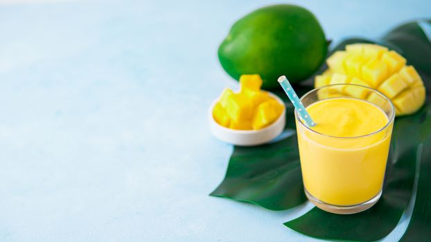 Yellow mango yogurt or smoothie on blue background with copy space left. Turmeric Lassie or lassi in glass. Banner