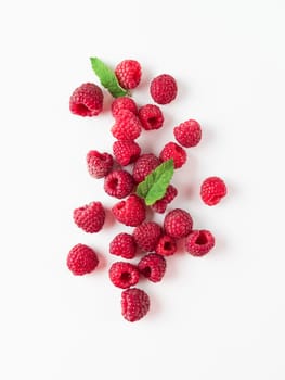 Heap of fresh ripe red raspberries with green leaves on white background. Top view or flat lay. Vertical