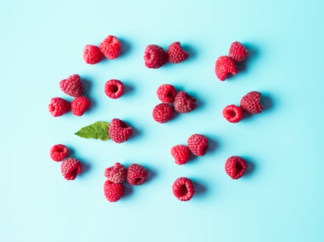 Pattern of ripe red raspberry on blue background. Creative layout of organic raspberries and green leaf. Top view or flat lay. Vegan food, detox concept