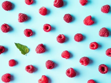 Pattern of ripe red raspberry on blue background. Creative layout of organic raspberries and green leaf. Top view or flat lay. Vegan food, detox concept