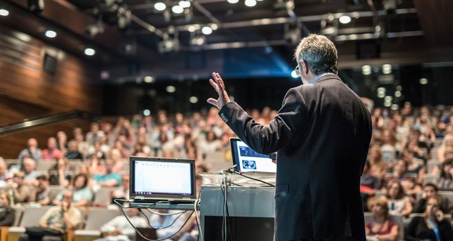 Speaker giving a talk on corporate business conference. Unrecognizable people in audience at conference hall. Business and Entrepreneurship event.