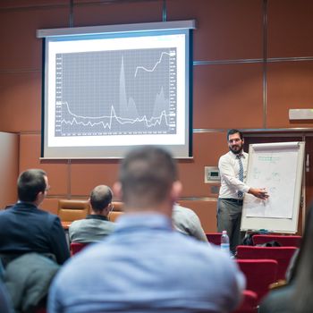 Public Speaker Giving a Talk at Business Meeting. Audience in the conference hall. Skilled coach answers questions of participants of business training. Business and Entrepreneurship concept.