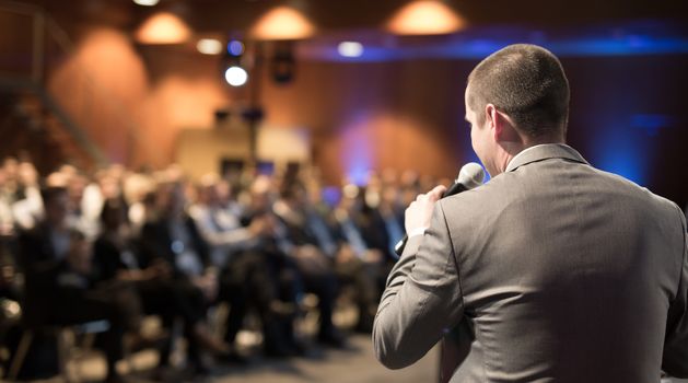 Speaker giving a talk on corporate business conference. Unrecognizable people in audience at conference hall. Business and Entrepreneurship event.