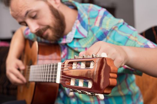 Bearded hipster man hand adjusting acoustic guitar. Close-up selective focus on hand.