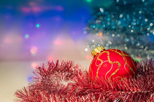 Red Christmas ball under the tree and tinsel on the background lights