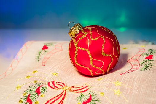 Red Christmas ball on festive napkin with embroidery on blue background