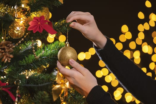 Girl decorates a Christmas tree. Closeup image of female hands decorating Christmas tree.